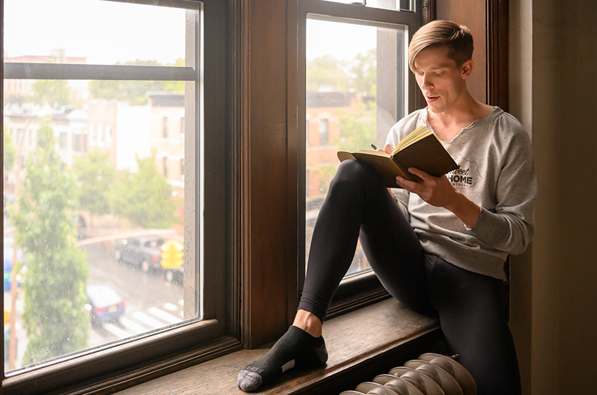 Chad is sitting on a windowsill reading a book.