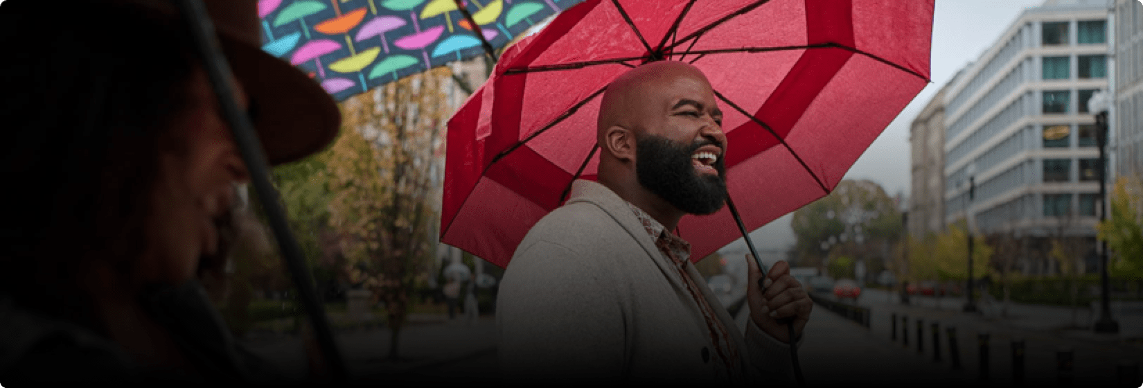 Phil is laughing outside while holding an umbrella.